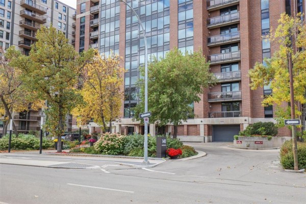Driveway entrance to a brick apartment building with autumn foliage. - 703 141 Wellington Crescent, Winnipeg