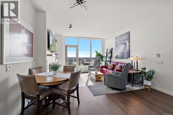 Living and dining area with hardwood floors, leather furniture, and large windows. - 703 4011 Rainbow Hill Lane, Saanich