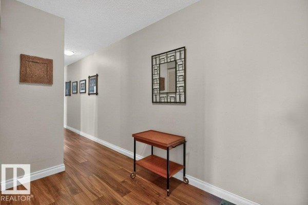Interior hallway with wood flooring, beige walls, and decorative mirror. - #703 9921 104 St Nw, Edmonton