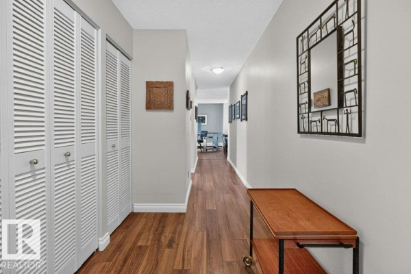 Interior hallway with white louvered doors, wood flooring, and beige walls. - #703 9921 104 St Nw, Edmonton