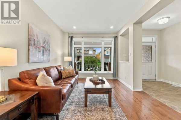 Living room with a brown leather sofa, coffee table, rug, and a large window overlooking the backyard. - 703 Mashkig Avenue E, Ottawa
