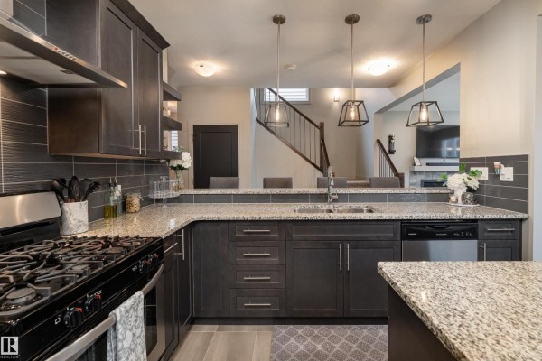 Kitchen featuring a gas range, granite countertops, dark wood cabinets, and a view towards the dining area. - 7038 172a Av Nw, Edmonton