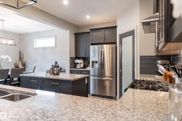 Kitchen space with granite island, stainless steel refrigerator, dark cabinets, and an adjacent dining area view. - 7038 172a Av Nw, Edmonton