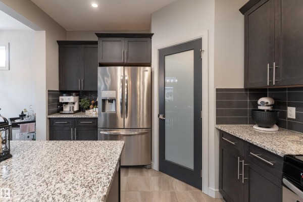 Stainless steel refrigerator and dark kitchen cabinets with granite countertops and a frosted glass door. - 7038 172a Av Nw, Edmonton