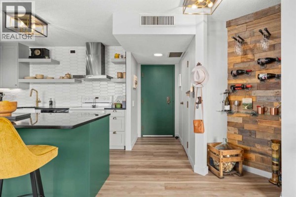 Kitchen island with seating, facing a stainless steel range hood and white backsplash tiles. - 704, 1202 13 Avenue Sw, Calgary