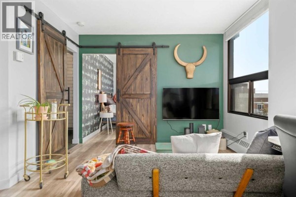 Living room with a gray sofa, wooden barn doors, and a television mounted on a green wall. - 704, 1202 13 Avenue Sw, Calgary