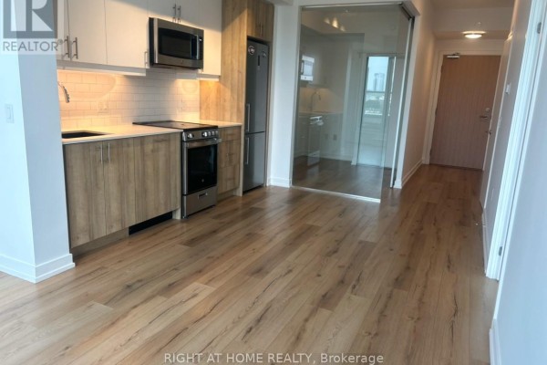 Open concept living space with light wood floors and a compact kitchen with stainless steel appliances. - 704 - 1195 The Queensway, Toronto