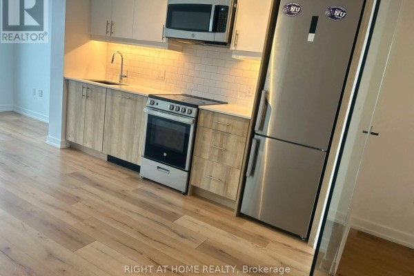 View of the kitchen area showing white subway tile backsplash and light wood cabinetry with stainless steel fridge. - 704 - 1195 The Queensway, Toronto