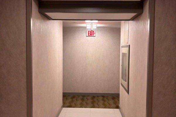 Hallway with light pink textured walls and a red exit sign. - 704 - 56 Annie Craig Drive, Toronto