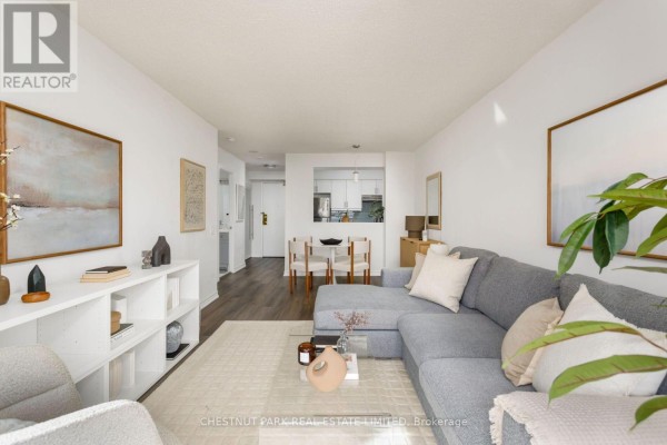 View of living room with sofa, white bookshelf, and entrance to kitchen and dining area. - 704 - 650 Lawrence Avenue W, Toronto
