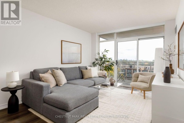 Living room with grey sectional sofa, armchair, and balcony access through sliding glass doors. - 704 - 650 Lawrence Avenue W, Toronto