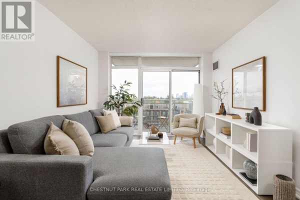 Living room with large grey sectional sofa, white bookshelf, and balcony access with city view. - 704 - 650 Lawrence Avenue W, Toronto