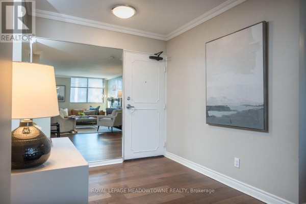Entryway with hardwood floors, large mirror, white door, and abstract wall art. - 704 - 81 Millside Drive, Milton