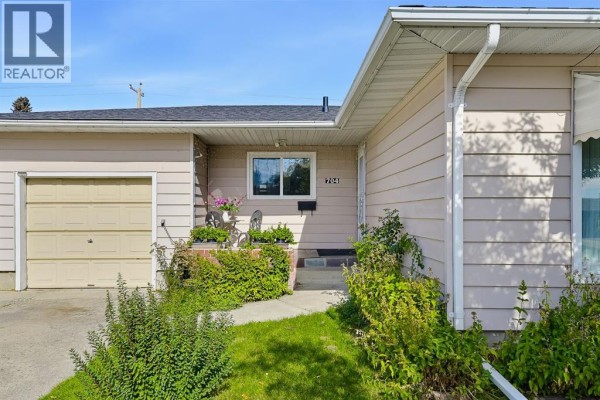 Close-up view of the house entrance with a beige garage door and colorful plants. - 704 75 Avenue Sw, Calgary