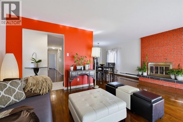 Living room with an orange accent wall, brick fireplace, and a view into the dining area. - 704 75 Avenue Sw, Calgary