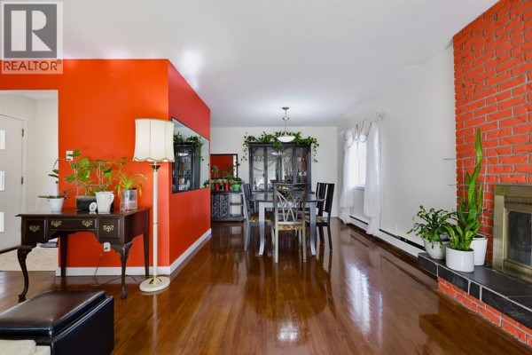 Spacious living and dining area with glossy hardwood floors, an orange accent wall, and a brick fireplace. - 704 75 Avenue Sw, Calgary