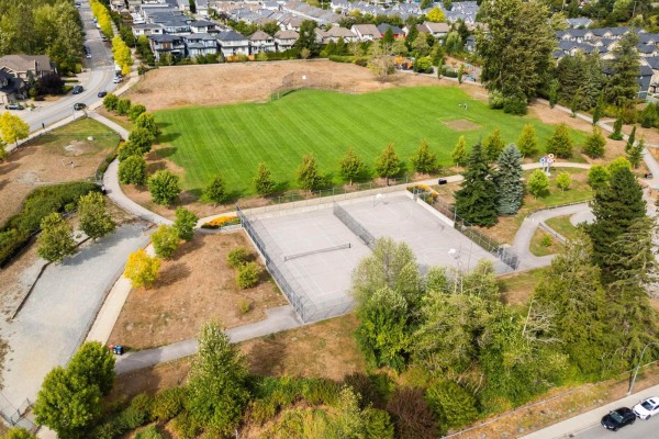 Aerial view of a park with a sports field, basketball courts, tennis courts, and surrounding trees and paths. - 7041 198a Street, Langley