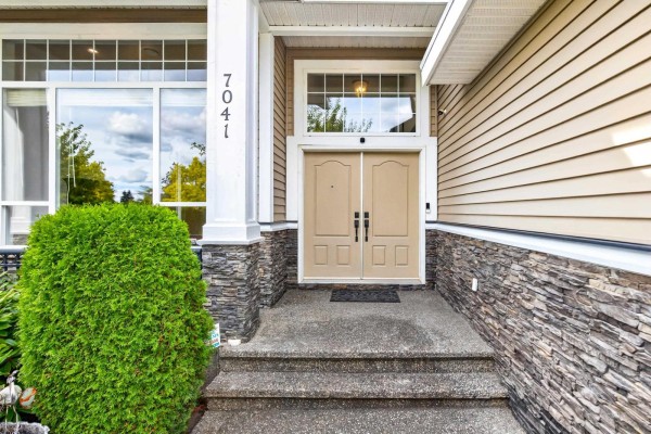 Close-up of the entrance to a beige house with double doors, stone accents, and concrete steps. - 7041 198a Street, Langley