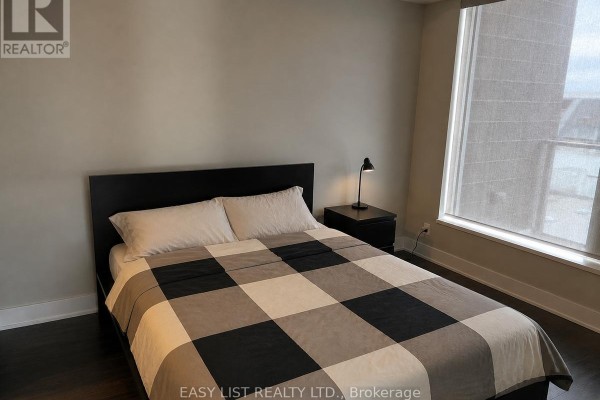 Living room with a white sofa, desk with computer, piano, and large windows. - 705 - 118 Holmwood Avenue, Ottawa