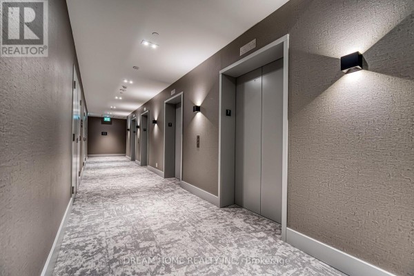A hotel-style hallway with elevators, modern lighting, and textured walls. - 705 - 285 Dufferin Street, Toronto