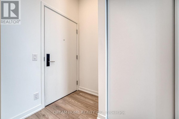 An apartment entrance with a white door, black hardware, and light wood flooring. - 705 - 285 Dufferin Street, Toronto
