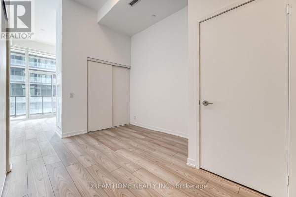 A bedroom with sliding closet doors, light wood flooring, and a door to a balcony. - 705 - 285 Dufferin Street, Toronto