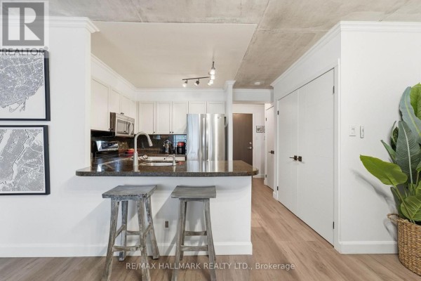Modern black kitchen with stainless steel appliances, white backsplash, and wooden floors. - 705 - 600 Queens Quay W, Toronto