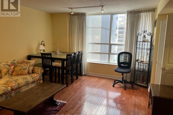 Living area with dining table, chairs, large window, and rolling office chair. - 705 - 71 Simcoe Street, Toronto