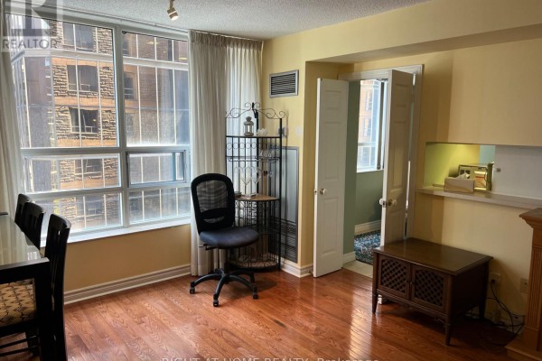 Living area with large windows, desk chair, doorway to another room, and cabinet. - 705 - 71 Simcoe Street, Toronto