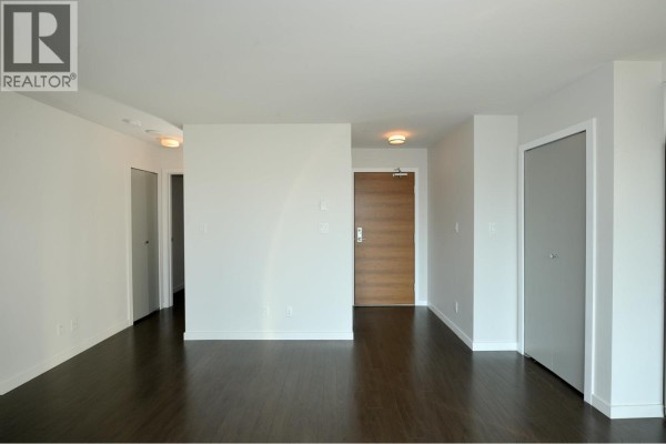View of a modern kitchen with dark cabinetry and stainless steel appliances extending into a living area. - 705 161 W Georgia Street, Vancouver