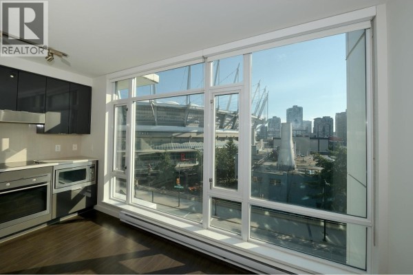 Kitchenette area with dark cabinets and stainless steel appliances against a large window with city views. - 705 161 W Georgia Street, Vancouver