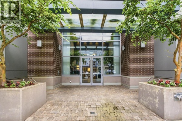 Building entrance with brick facade, glass doors, and trees in concrete planters. - 705 538 W 7th Avenue, Vancouver