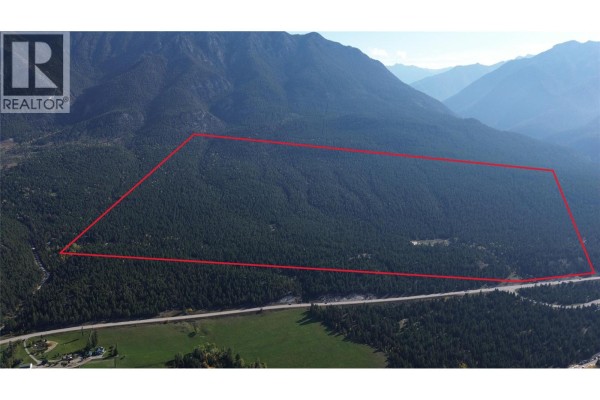 Aerial view of a large parcel of land outlined in red, covered in trees, adjacent to a highway. - 7058 95 Highway, Radium Hot Springs