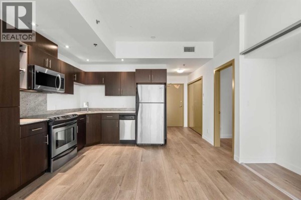 View of the kitchen area with dark wood cabinets, stainless steel appliances, and polished concrete floors. - 706, 135 13 Avenue Sw, Calgary