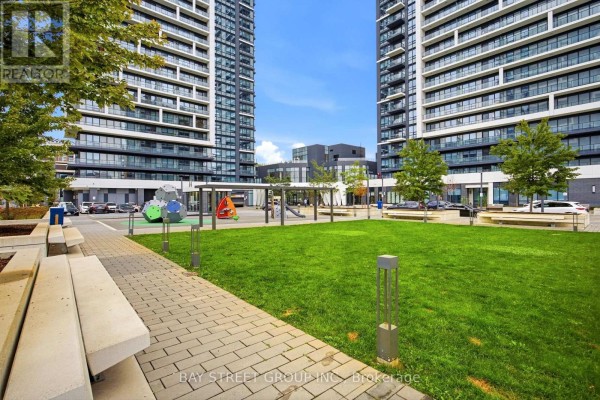 Green lawn and brick pathway with playground equipment and concrete benches. - 706 - 18 Water Walk Drive, Markham