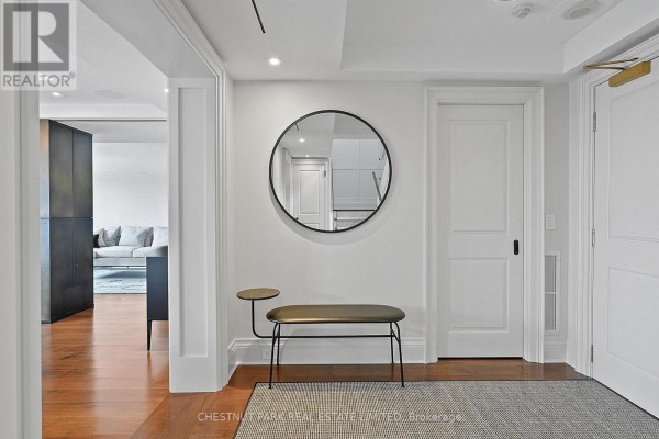 Hallway with hardwood floors, a round mirror, a bench, and two white doors. - 706 - 1818 Bayview Avenue, Toronto