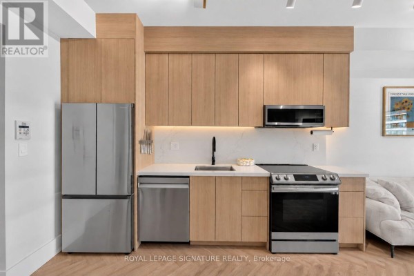 Close-up of the kitchen area with light wood cabinets, stainless steel appliances, and a black faucet. - 706 - 33 Shore Breeze Drive, Toronto