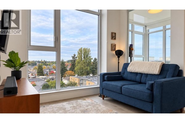 Blue sofa in living area with a large window view of surrounding houses and trees. - 706 2435 Kingsway, Vancouver