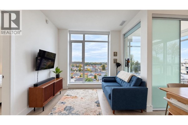 Living area with blue sofa, wooden media console, flat screen TV, and patterned rug. - 706 2435 Kingsway, Vancouver