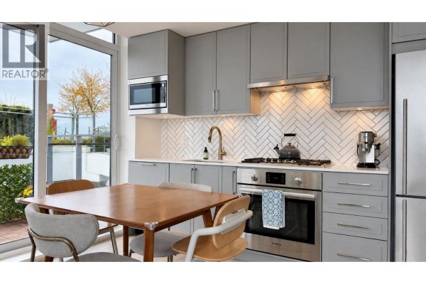 Kitchen with grey cabinets, stainless steel appliances, white herringbone backsplash, and wood dining table. - 706 2435 Kingsway, Vancouver