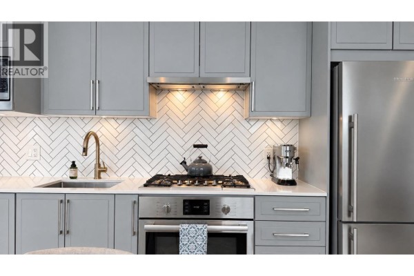 Close-up of a kitchen with grey cabinets, stainless steel sink, gas stove, and stainless steel refrigerator. - 706 2435 Kingsway, Vancouver
