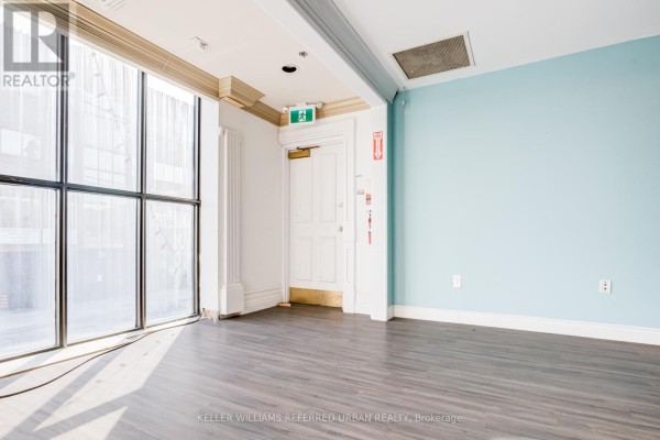 A large window with black muntins lets sunlight into an empty room with blue walls and wood flooring. - 706 Pape Avenue, Toronto