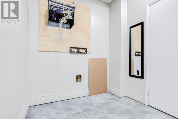 A wall with exposed wiring and a metal electrical box above a mirror with a black frame. - 706 Pape Avenue, Toronto