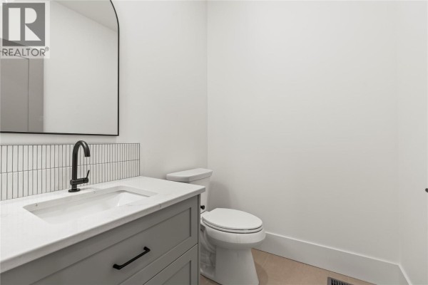 Powder room with a white vanity, grey drawers, black faucet, and white tiled backsplash. - 7060 Manning Place, Vernon