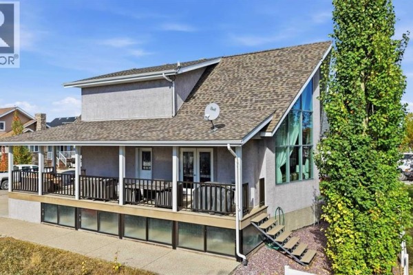 Exterior of a grey stucco house with a covered deck, large windows, and a peaked roof. - 7062, 35468 Range Road 30, Rural Red Deer County