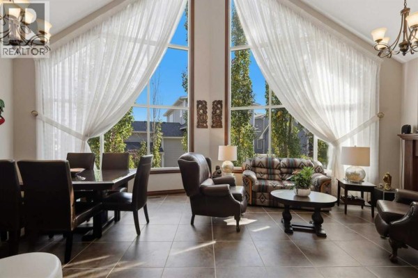 Living room with a dining table, leather chairs, patterned sofa, and large arched windows with white curtains. - 7062, 35468 Range Road 30, Rural Red Deer County
