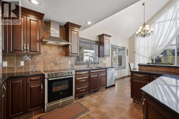 Dark wood kitchen cabinetry, stainless steel appliances, granite countertops, and tiled backsplash and flooring. - 7062, 35468 Range Road 30, Rural Red Deer County