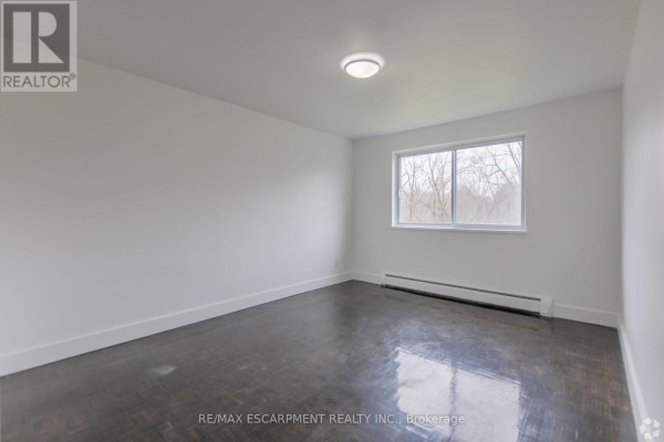 An empty bedroom with dark hardwood floors and a large window. - 707 - 285 Erb Street W, Waterloo