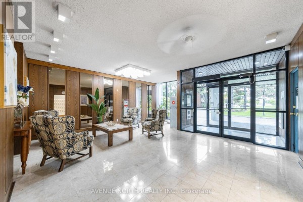 Lobby area with patterned armchairs, wooden paneling, mirrored walls, and marble tile flooring. - 707 - 3360 Southgate Road, Ottawa