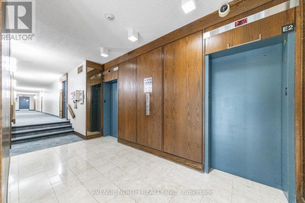 Hallway with elevator doors, wooden wall paneling, and a carpeted staircase leading down the corridor. - 707 - 3360 Southgate Road, Ottawa